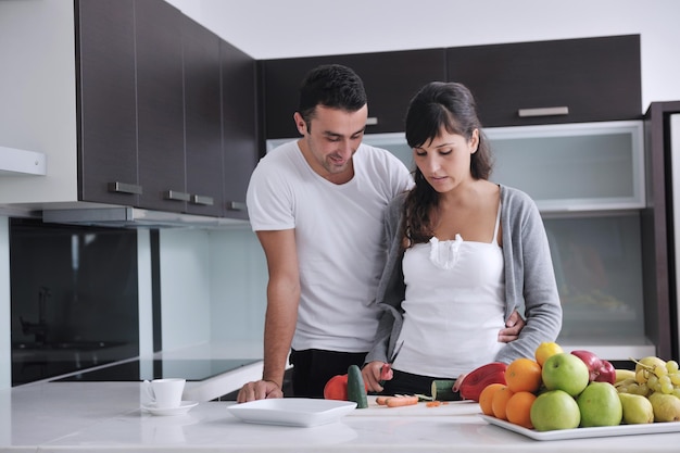 feliz pareja joven se divierte en la cocina moderna interior mientras prepara ensalada de frutas y verduras frescas