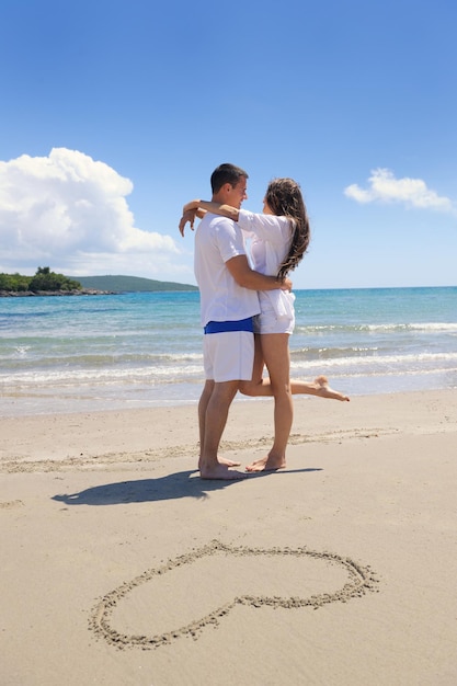 feliz pareja joven diviértete y relájate en el verano con el corazón dibujando en la arena de la playa