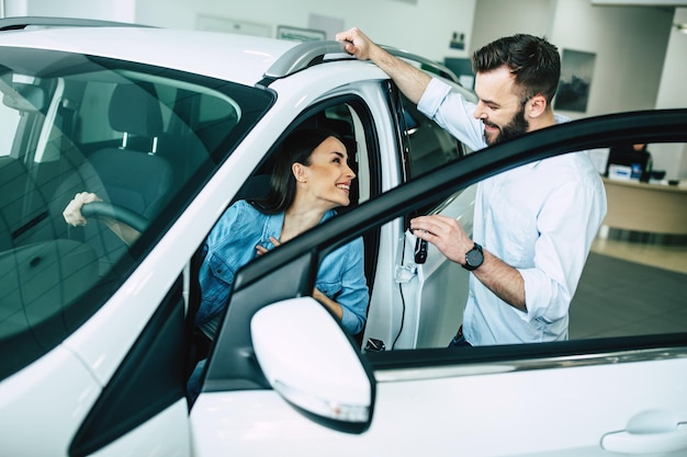 Feliz pareja joven elige y compra un auto nuevo para la familia en el concesionario