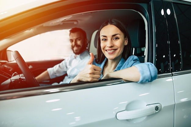 Feliz pareja joven elige y compra un auto nuevo para la familia en el concesionario