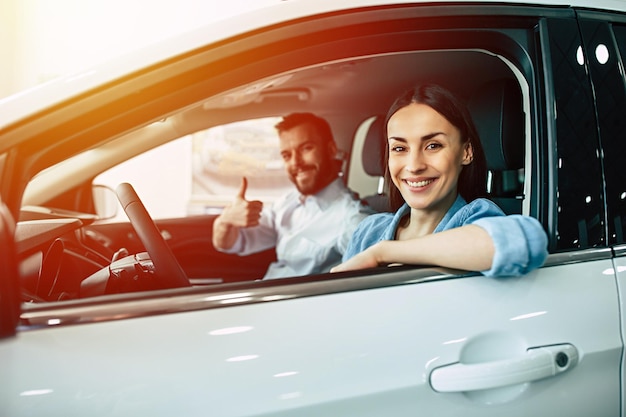 Feliz pareja joven elige y compra un auto nuevo para la familia en el concesionario