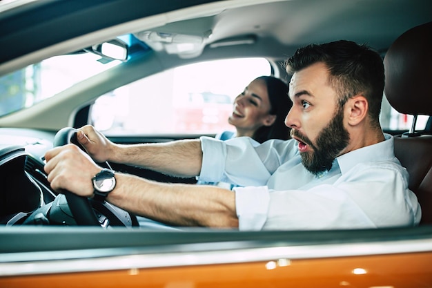 Feliz pareja joven elige y compra un auto nuevo para la familia en el concesionario