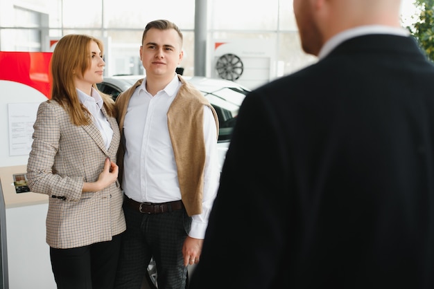 Feliz pareja joven elige y compra un coche nuevo para la familia en el concesionario.