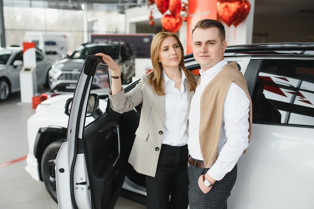 Foto feliz pareja joven elige y compra un coche nuevo para la familia en el concesionario.