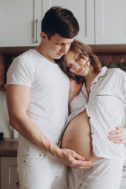 Feliz pareja joven embarazada pijama blanco sosteniendo un bulto en la por la