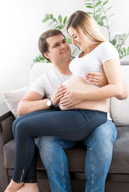 Feliz pareja joven embarazada sonriendo y mirando el vientre grande