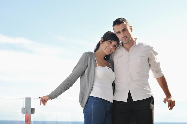 feliz pareja joven enamorada tiene romance relajarse en el balcón al aire libre con el océano y el cielo azul en segundo plano