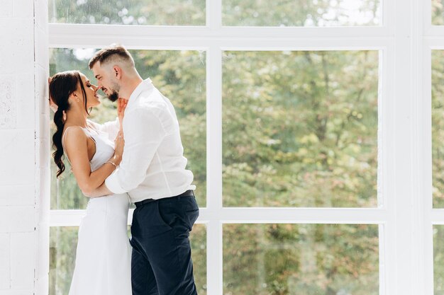 Feliz pareja joven encantadora de pie junto a la ventana en casa