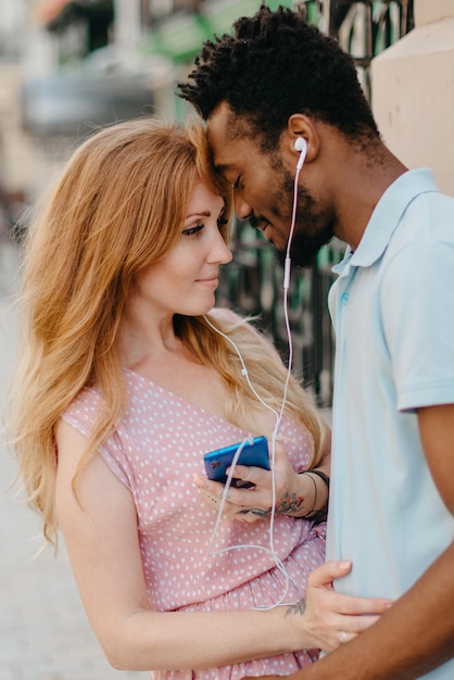 Feliz pareja joven escuchando música junto con auriculares en una calle de la ciudad en un día soleado