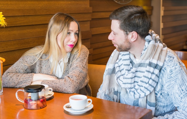 Feliz pareja joven está hablando y tomando café y sonriendo mientras está sentado en el café.