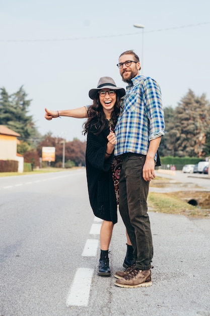 Feliz pareja joven hermosa haciendo autostop al aire libre divirtiéndose a través de pasajes