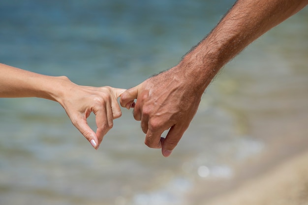 Feliz pareja joven hombre y mujer tomados de la mano y relajarse juntos en la playa. Contra el agua de mar en la playa, de cerca. Concepto de amor y vacaciones de viajes de verano