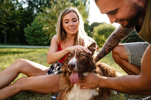 Feliz pareja joven jugando con su perro sonriendo en el parque