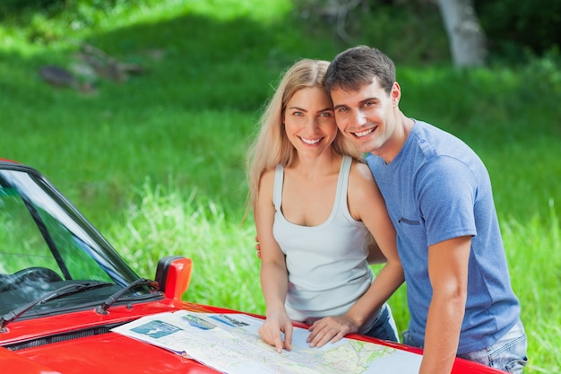 Feliz pareja joven leyendo mapa en su capó cabriolet