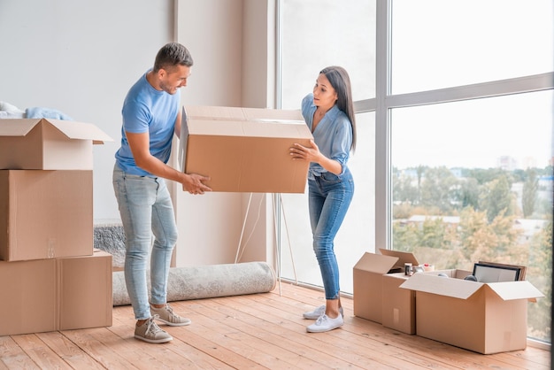 Feliz pareja joven llevando caja de mudanza y divirtiéndose