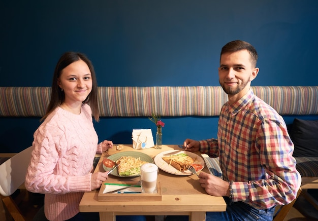 Feliz pareja joven mirando a la cámara mientras disfruta de una comida sabrosa en un pequeño café juntos Concepto de relación