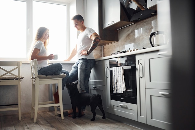 Feliz pareja joven moderna en la cocina de casa con su lindo perro.