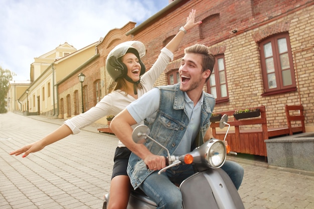 Feliz pareja joven montando scooter en la ciudad. Chico guapo y viaje de mujer joven. Concepto de aventura y vacaciones.