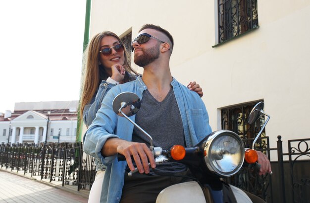 Feliz pareja joven montando scooter en la ciudad. Chico guapo y viaje de mujer joven. Concepto de aventura y vacaciones.