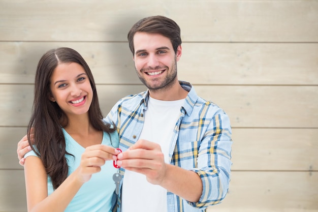 Feliz pareja joven mostrando la nueva llave de la casa contra el fondo de tablones de madera blanqueados