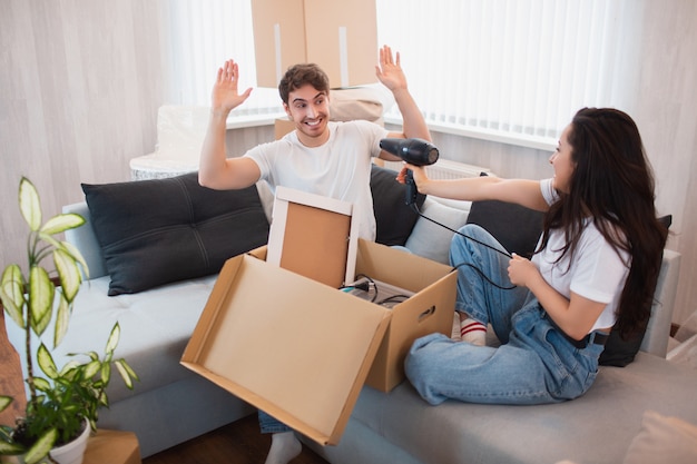 Feliz pareja joven mudarse a un nuevo hogar. Se divierten con los electrodomésticos mientras desempacan cosas.