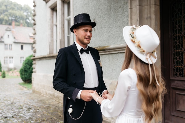 Feliz pareja joven Novias con sombreros Chica joven con un vestido de novia blanco y un sombrero con un ramo de flores Novias en el castillo Novia y novio