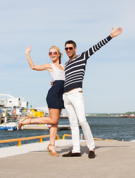 Feliz pareja joven de pie y saludando en el puerto