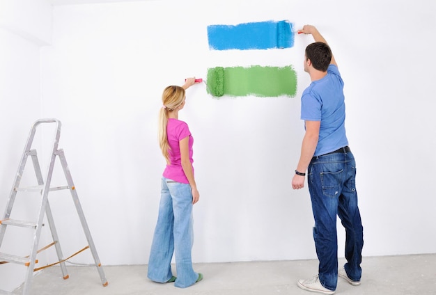 feliz pareja joven pinta en color verde y azul la pared blanca de su nuevo hogar