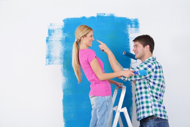 feliz pareja joven pinta en color verde y azul la pared blanca de su nuevo hogar