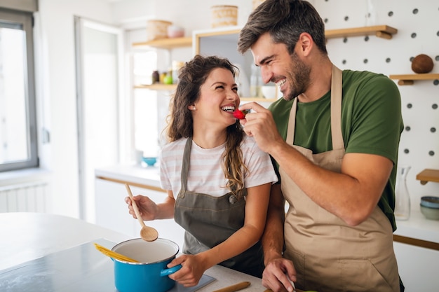 Feliz pareja joven preparando la comida en la cocina de casa. Comida sana, concepto de personas