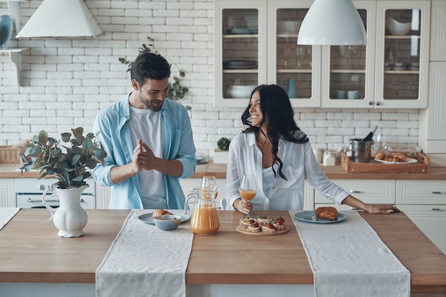 Feliz pareja joven preparando el desayuno juntos mientras pasan tiempo en la cocina doméstica