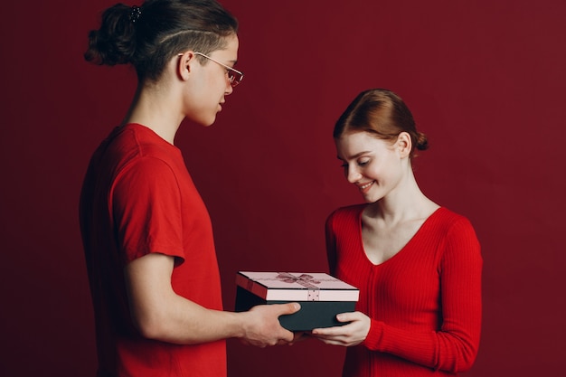 Feliz pareja joven con un presente aislado sobre fondo rojo.