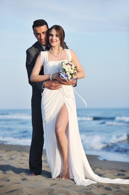 feliz pareja joven recién casada celebrando y divirtiéndose en la hermosa puesta de sol en la playa
