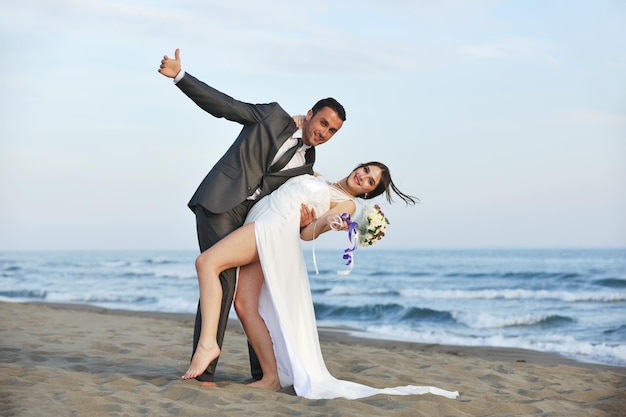 feliz pareja joven recién casada celebrando y divirtiéndose en la hermosa puesta de sol en la playa