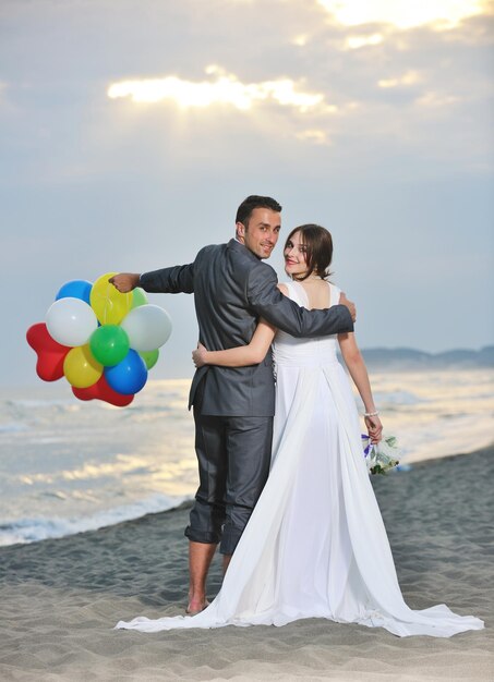 feliz pareja joven recién casada celebrando y divirtiéndose en la hermosa puesta de sol en la playa