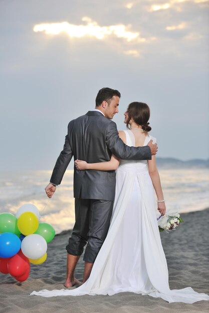 feliz pareja joven recién casada celebrando y divirtiéndose en la hermosa puesta de sol en la playa