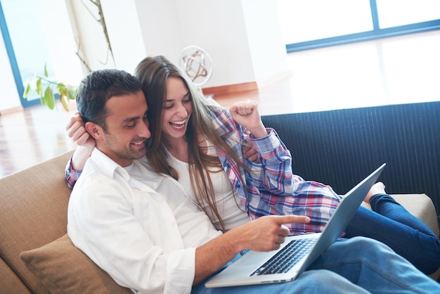 feliz pareja joven y relajada trabajando en una computadora portátil en el interior de una casa moderna
