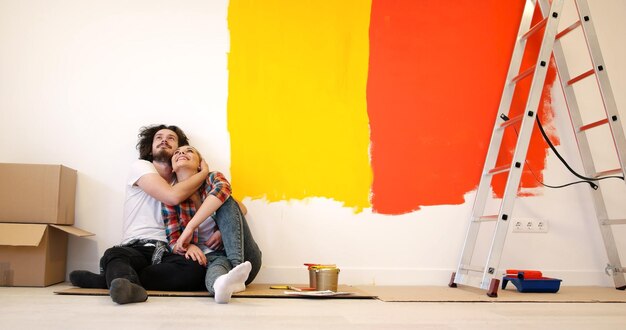 Feliz pareja joven relajándose después de pintar una habitación en su nueva casa en el suelo