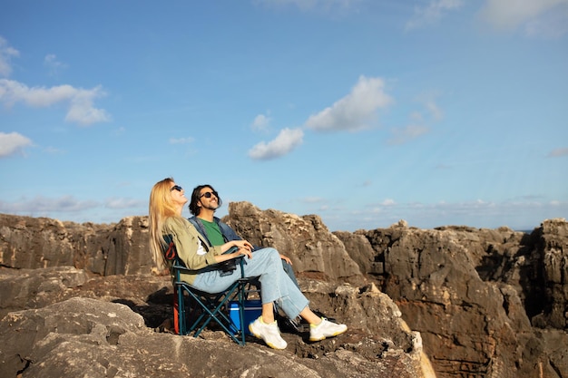 Feliz pareja joven relajándose en sillas de camping en la costa rocosa