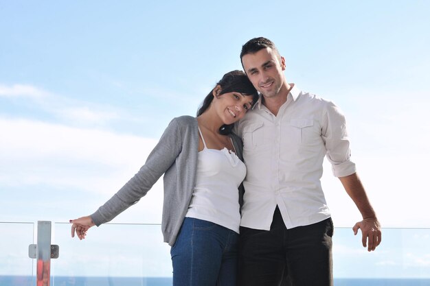 feliz pareja joven relajarse en el balcón al aire libre con el océano y el cielo azul de fondo