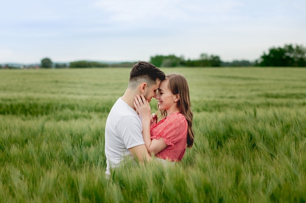 Feliz pareja joven romántica en un campo de cebada. chica con un vestido rojo y un chico. retrato de pareja caminando en la hierba.