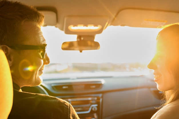 Feliz pareja joven en el salón de su auto nuevo al atardecerComprar un auto en el salón