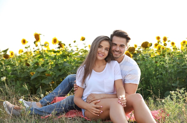 Feliz pareja joven sentada en el campo de girasoles