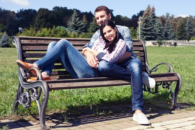 Feliz pareja joven sentada descansando en un banco del parque