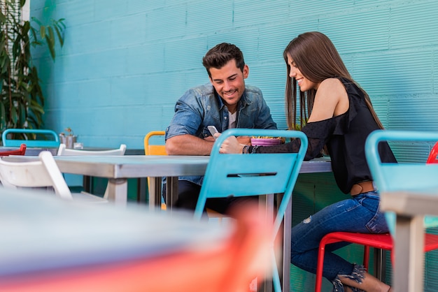 Feliz pareja joven sentado en un restaurante con un teléfono inteligente