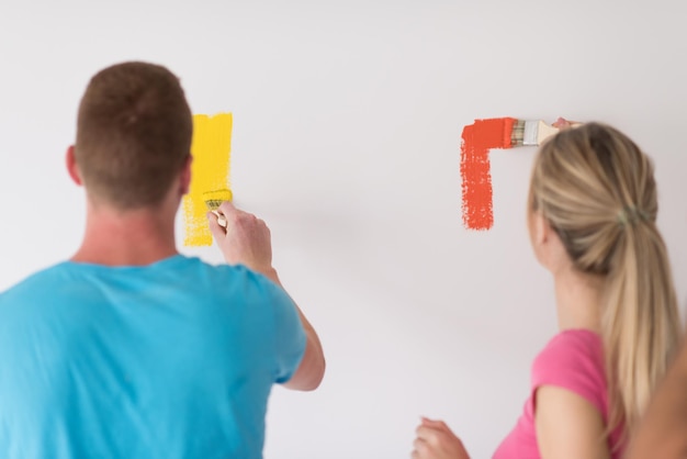 feliz pareja joven sonriente pintando la pared interior de la nueva casa