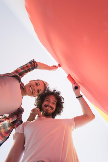 Foto feliz pareja joven sonriente pintando la pared interior de la nueva casa