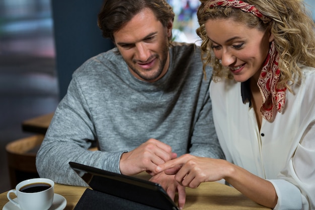 Feliz pareja joven con tablet PC en la mesa de la cafetería