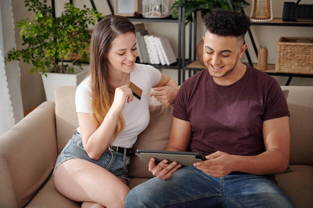 Feliz pareja joven con tarjeta de crédito haciendo compras online comprando ropa y zapatos a la venta en onli ...