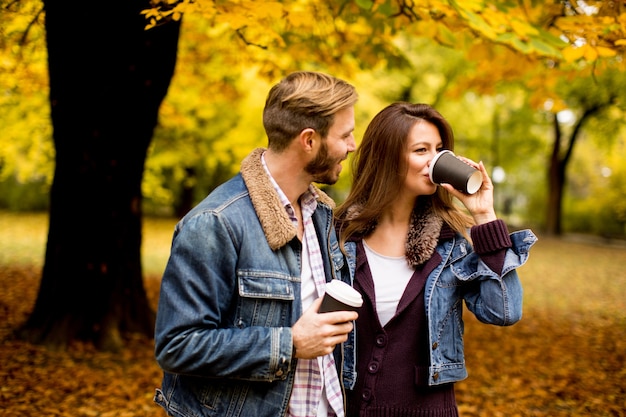 Feliz pareja joven con tazas de café caminando en el parque de otoño